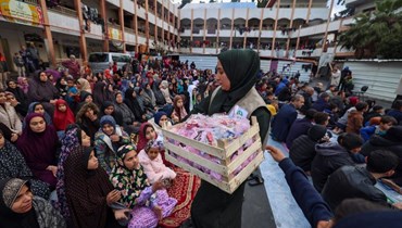 امرأة توزع الحلوى على الفلسطينيين النازحين أثناء حضورهم صلاة صباحية خاصة لبدء مهرجان عيد الفطر، بمناسبة نهاية شهر رمضان المبارك، في مدرسة تحولت إلى مأوى في رفح (أ ف ب).