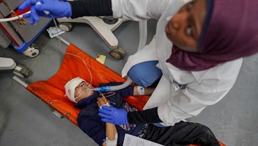 مسعفة تقدم الإسعافات الأولية لطفل مصاب يرقد على نقالة في مستشفى شهداء الأقصى في دير البلح، وسط غزة (16 نيسان 2024 - أ ف ب).