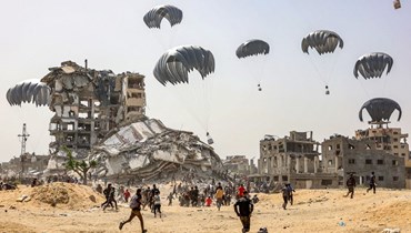أشخاص يسرعون صوب مساعدات إنسانية يتم إسقاطها فوق شمال قطاع غزة (23 نيسان 2024، أ ف ب).