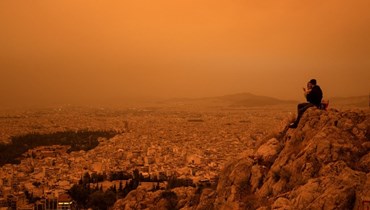 زوجان يجلسان على تلة توركوفونيا، بينما تحمل الرياح الجنوبية موجات من الغبار الصحراوي، في أثينا (23 نيسان 2024 - أ ف ب).