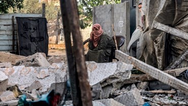 فتاة تنظر خلف امرأة جلست وسط الأنقاض في رفح بجنوب قطاع غزة (24 نيسان 2024، أ ف ب). 