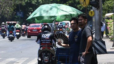 شخص يستعين بمروحة يدوية وسط حرارة شديدة، بينما ينتظر على  طريق في مانيلا (24 نيسان 2024، أ ف ب). 