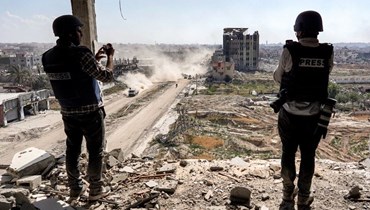 صحافيون يصورون من مبنى متضرر يواجه مبنى مستشفى السلام المدمر في خان يونس بعدما سحبت إسرائيل قواتها البرية من جنوب قطاع غزة (7 نيسان 2024، أ ف ب).