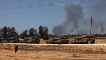 دبابات إسرائيلية تمركزت في جنوب إسرائيل قرب الحدود مع قطاع غزة بينما تصاعد الدخان فوق غزة خلال قصف إسرائيلي (7 ايار 2024، أ ف ب). 