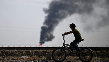 شاب عراقي يمر بدراجته قرب حقل الرميلة النفطي بجوار مدينة البصرة الساحلية جنوب العراق (5 ايار 2024، أ ف ب). 