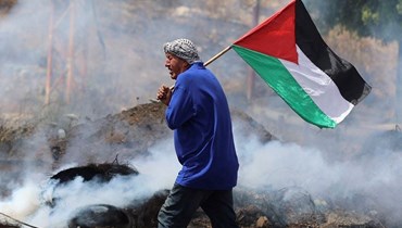 متظاهر فلسطيني يرفع العلم الفلسطيني خلال مواجهات مع القوات الإسرائيلية عند حاجز حوارة جنوب مدينة نابلس بالضفة الغربية المحتلة (21 ايار 2021، أ ف ب). 